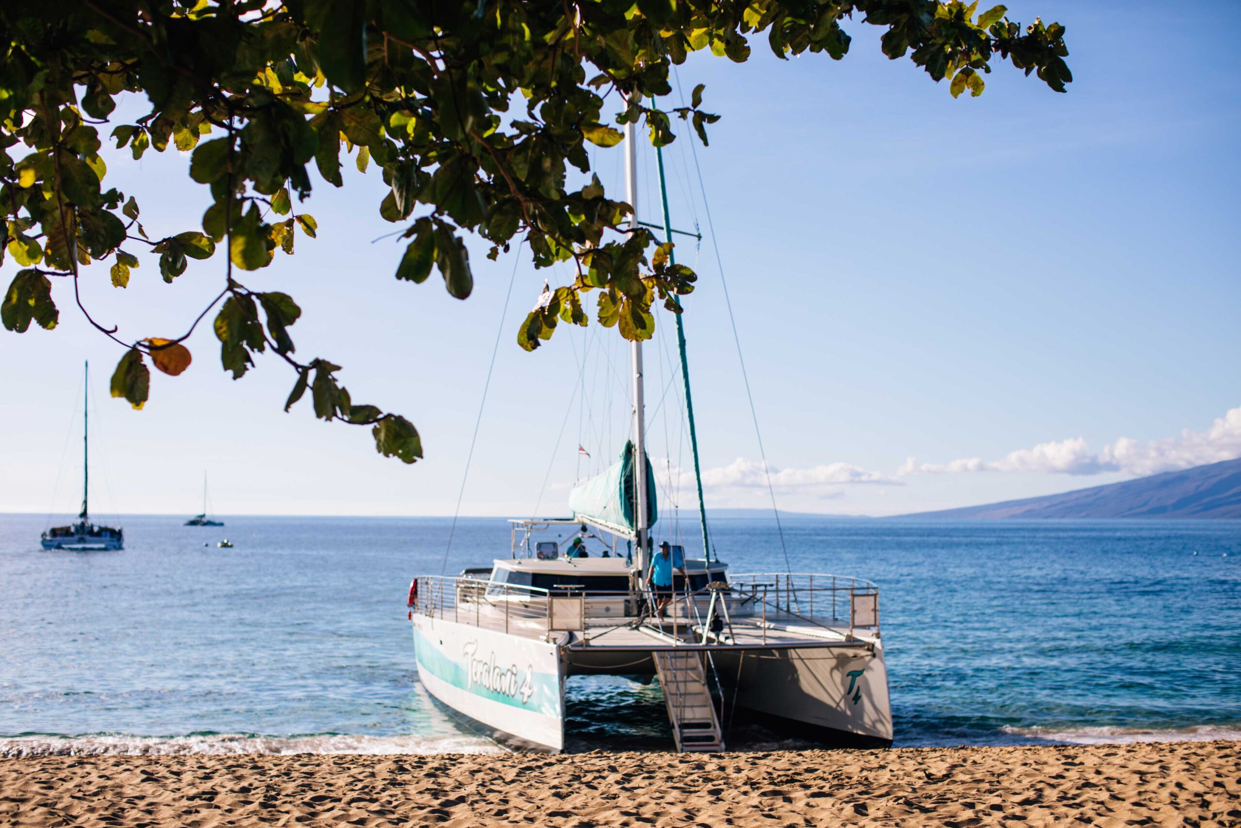 Sandy beach with a beached sailboat waiting to embark with other sailboats in the background