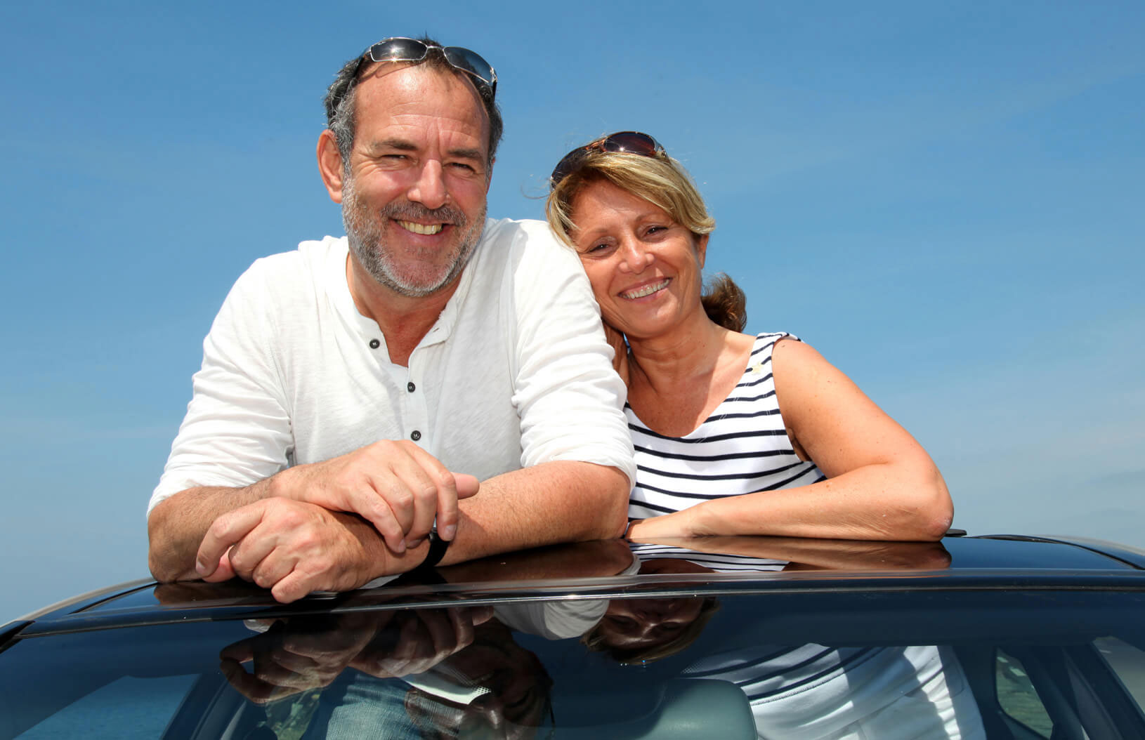 A man and woman smiling while standing in the sunroof of their car