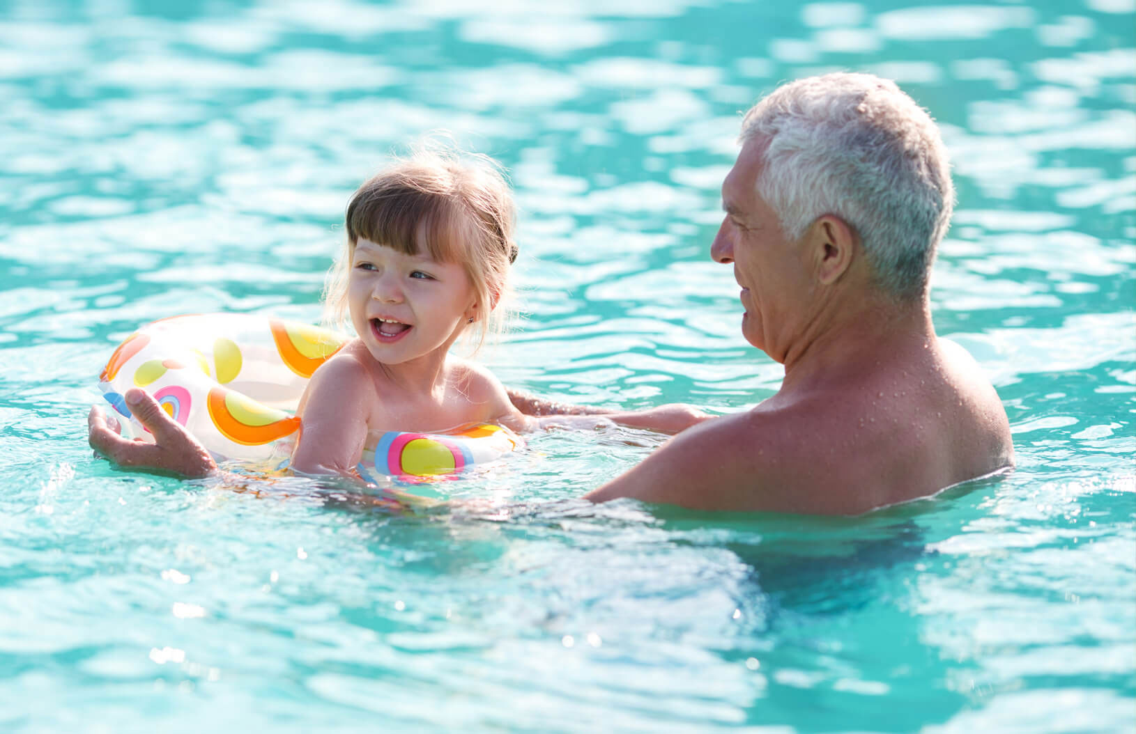 Grandfather and granddaughter in a inflatable inner-tube playing in a pool