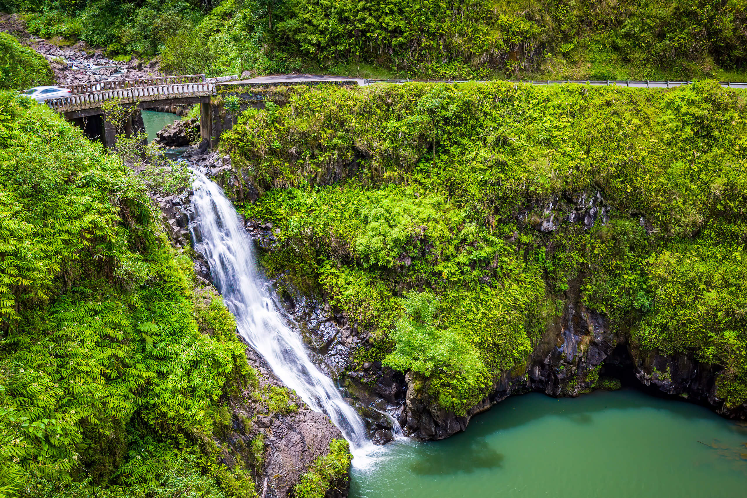 car driving over bridge along scenic landscape with waterfall